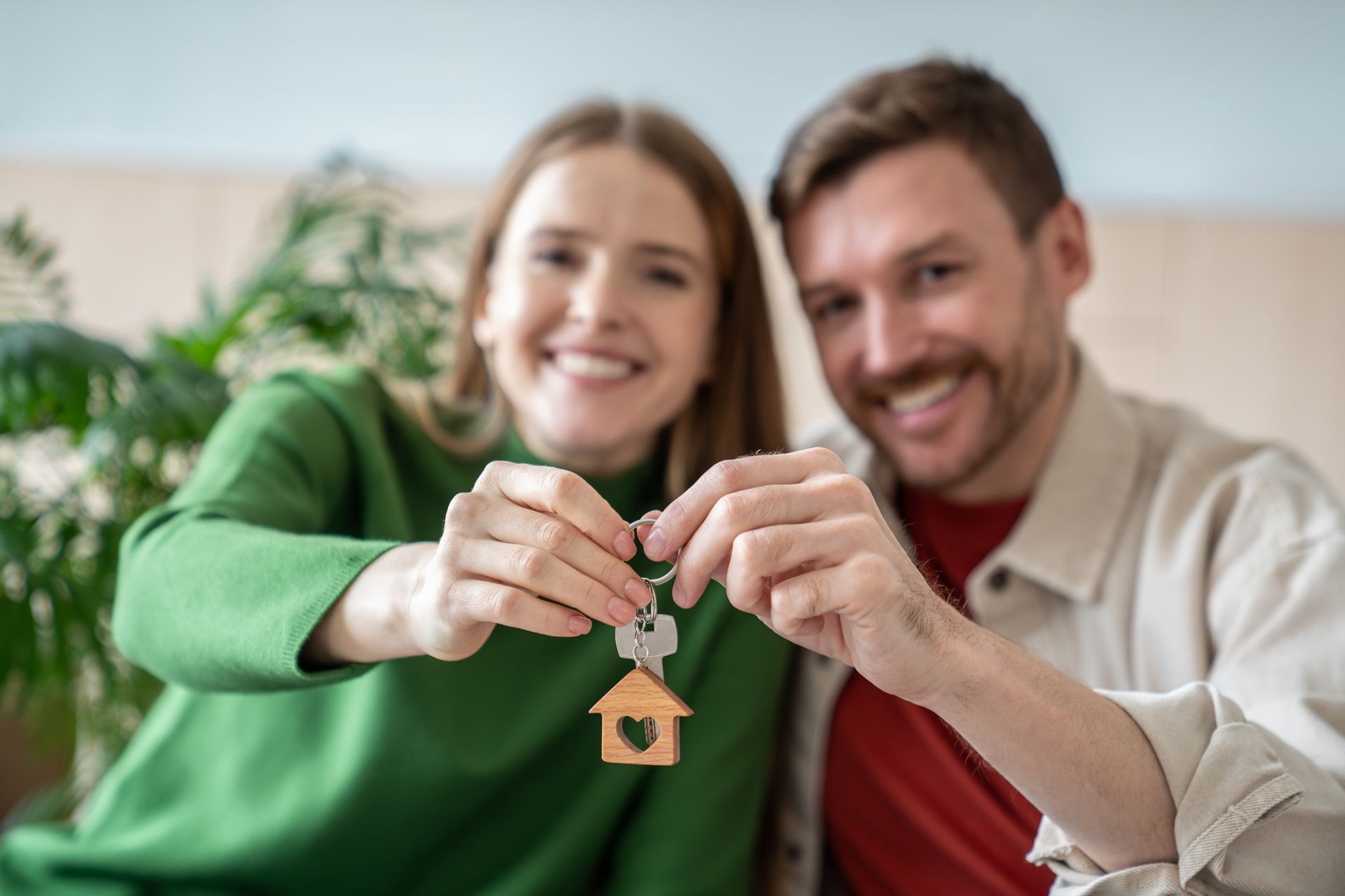 Smiling couple holding keys with a house-shaped keychain, symbolizing buying a new home.
