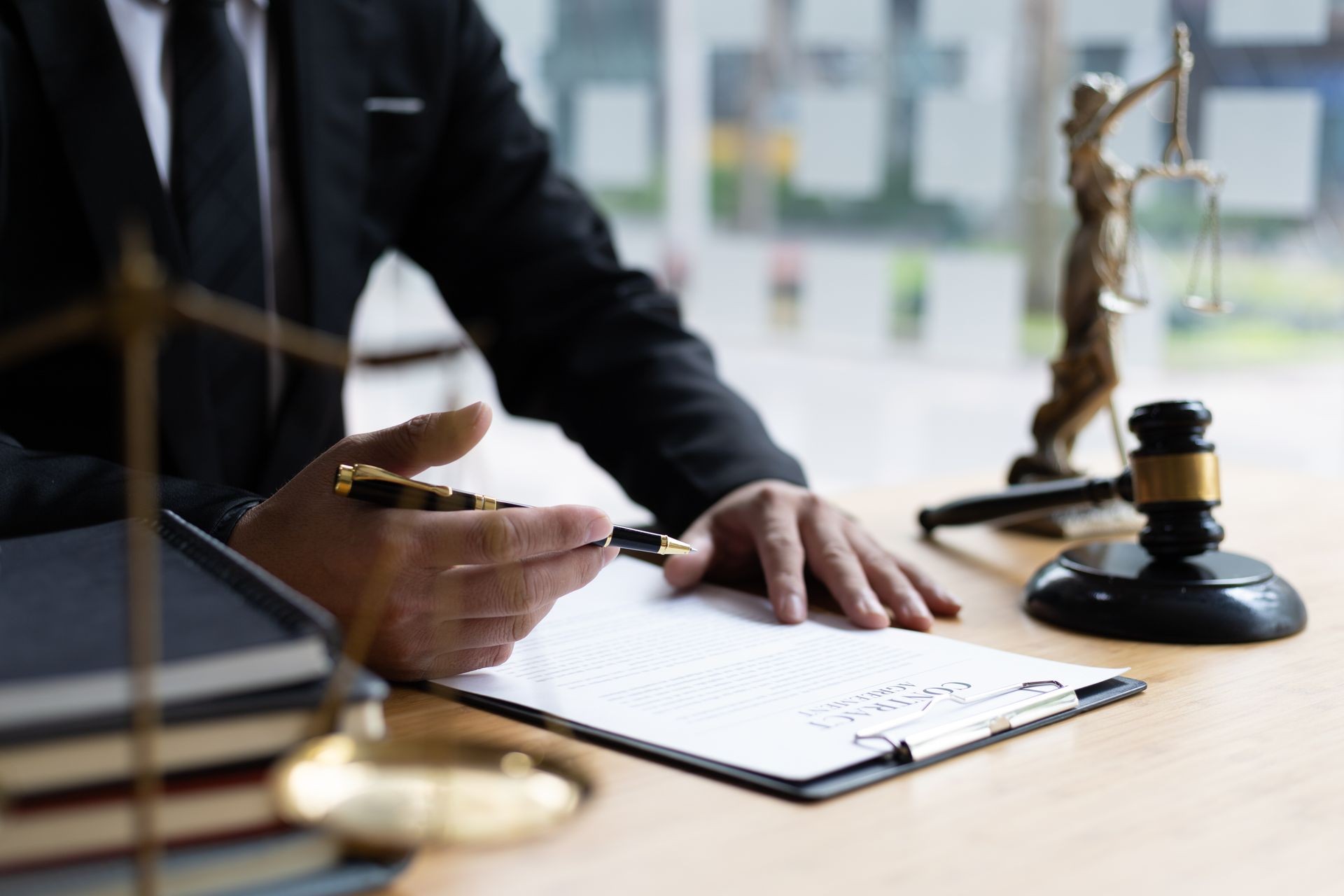 Person in a suit reviewing a legal document at a desk with a gavel and justice statue.