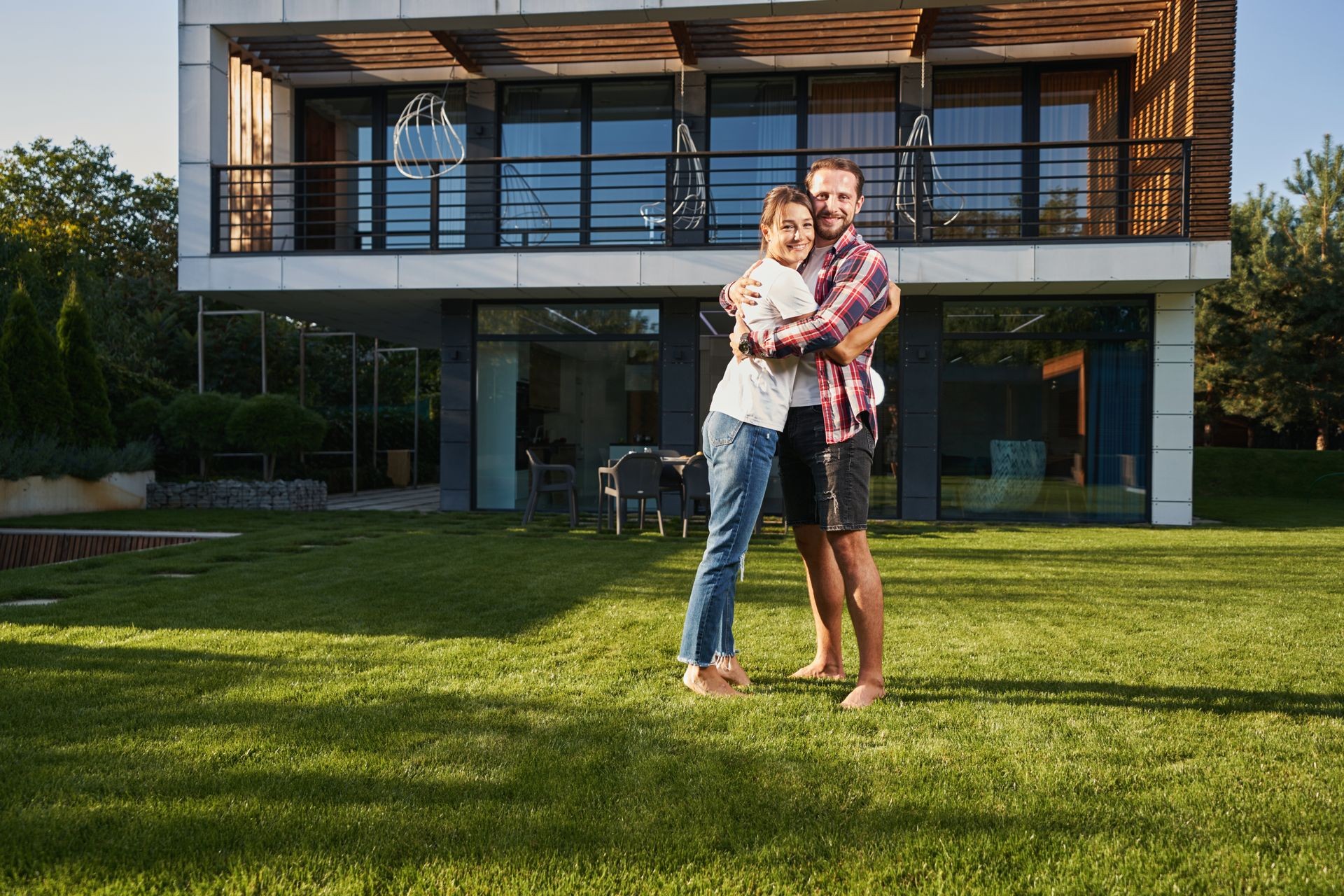 A couple happily embracing in the garden in front of a modern two-story house.